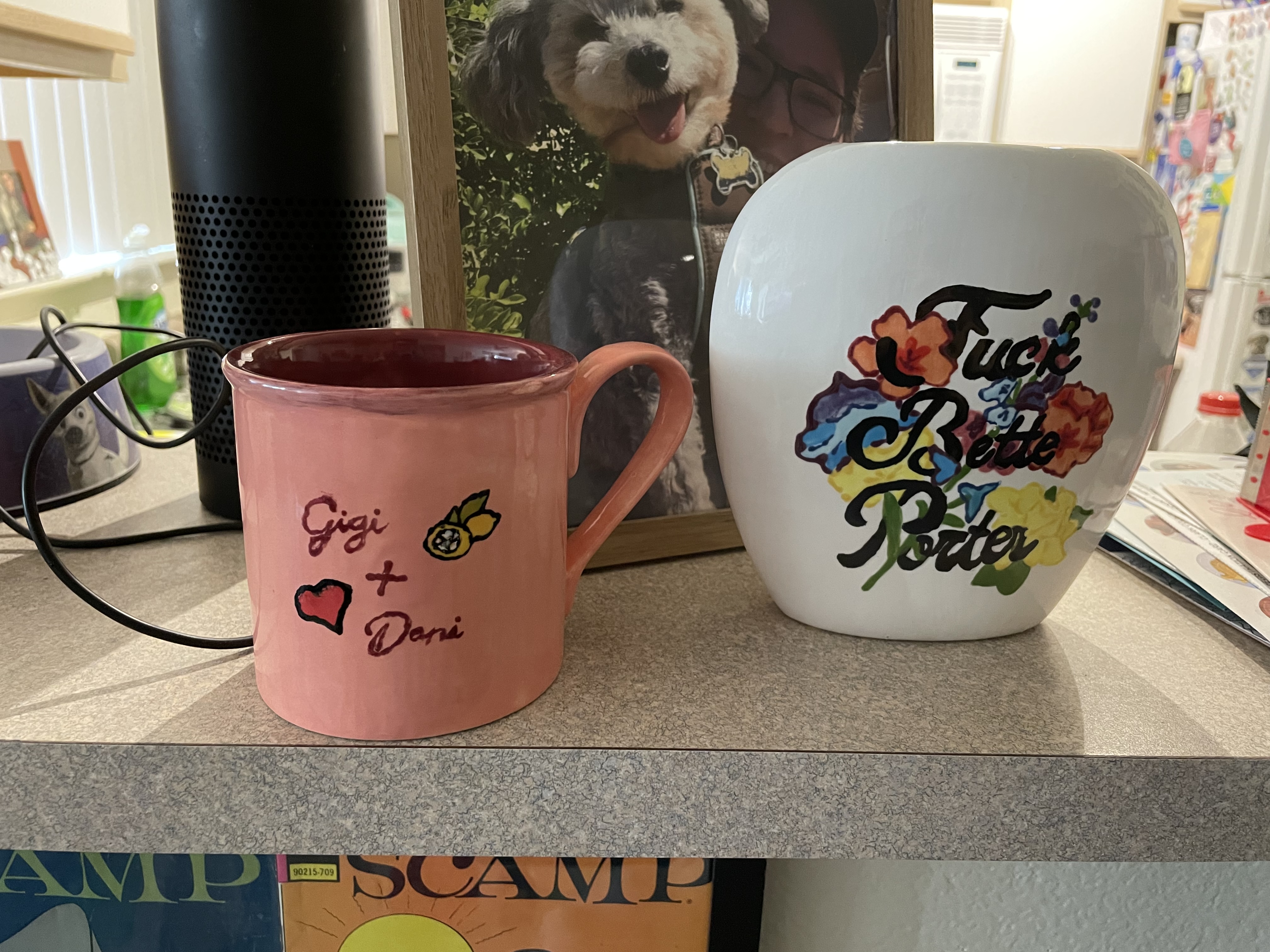 This is the first view of two pieces of pottery. On the left is a mug that says "Gigi + Dani" and which has a heart on it. On the right is a vase that says "Fuck Bette Porter" over a floral background.