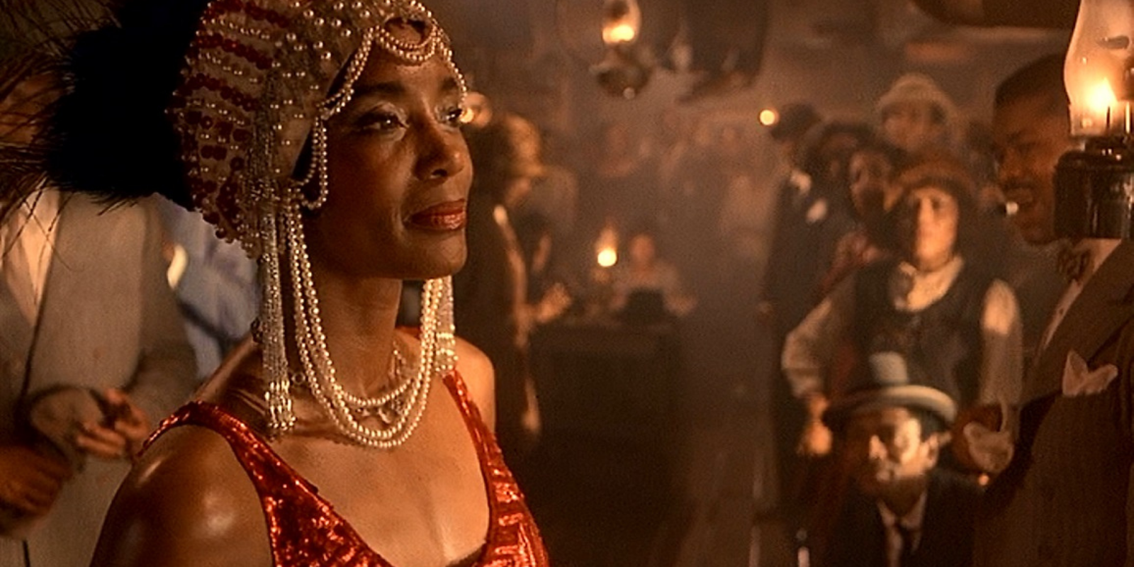 Shug stands on stage, decked out in a pearl headpiece, with her head held high as others look at her ready to perform.