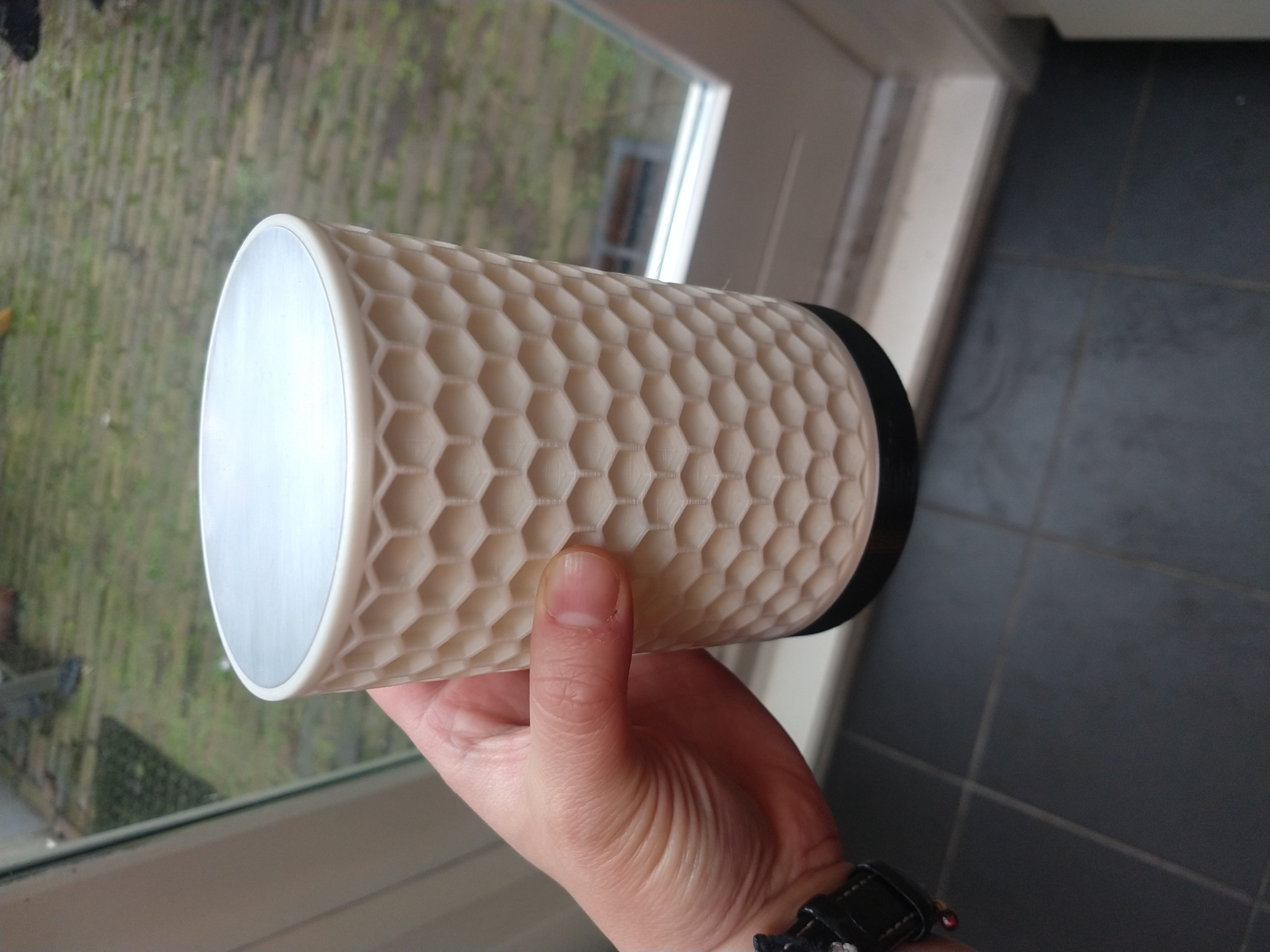 A pale hand holding one of the lamps. It has an off-white honeycomb pattern.