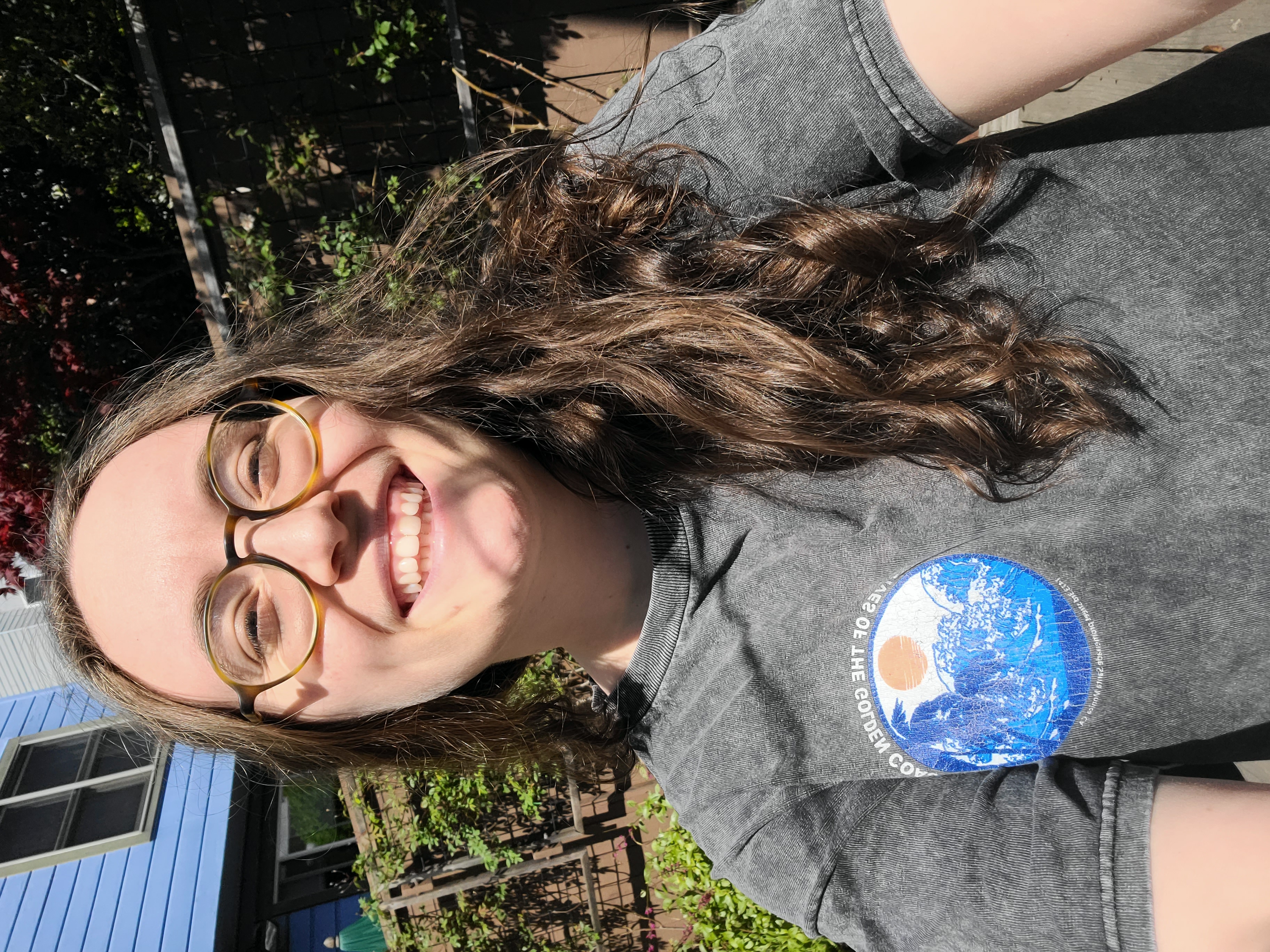 Anya, a white woman with glasses and long brown hair, is wearing a shirt with a little west coast looking graphic on it.