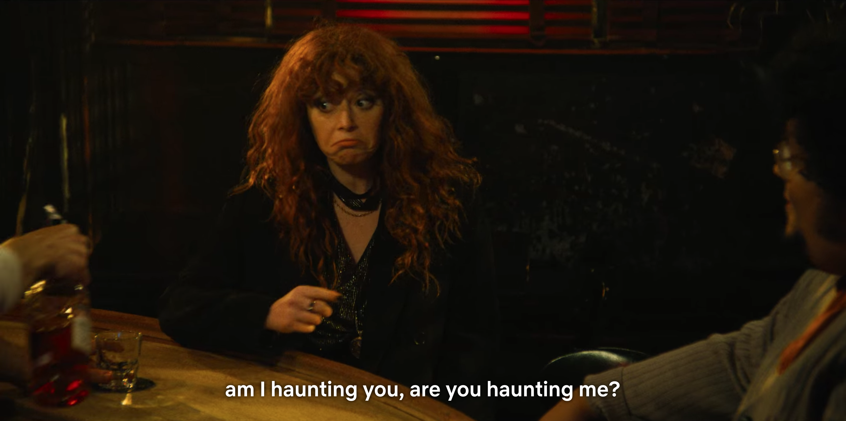 Natasha Lyonne as Nadia sits at a bar, asking "am I haunting you, are you haunting me?" in Russian Doll season two