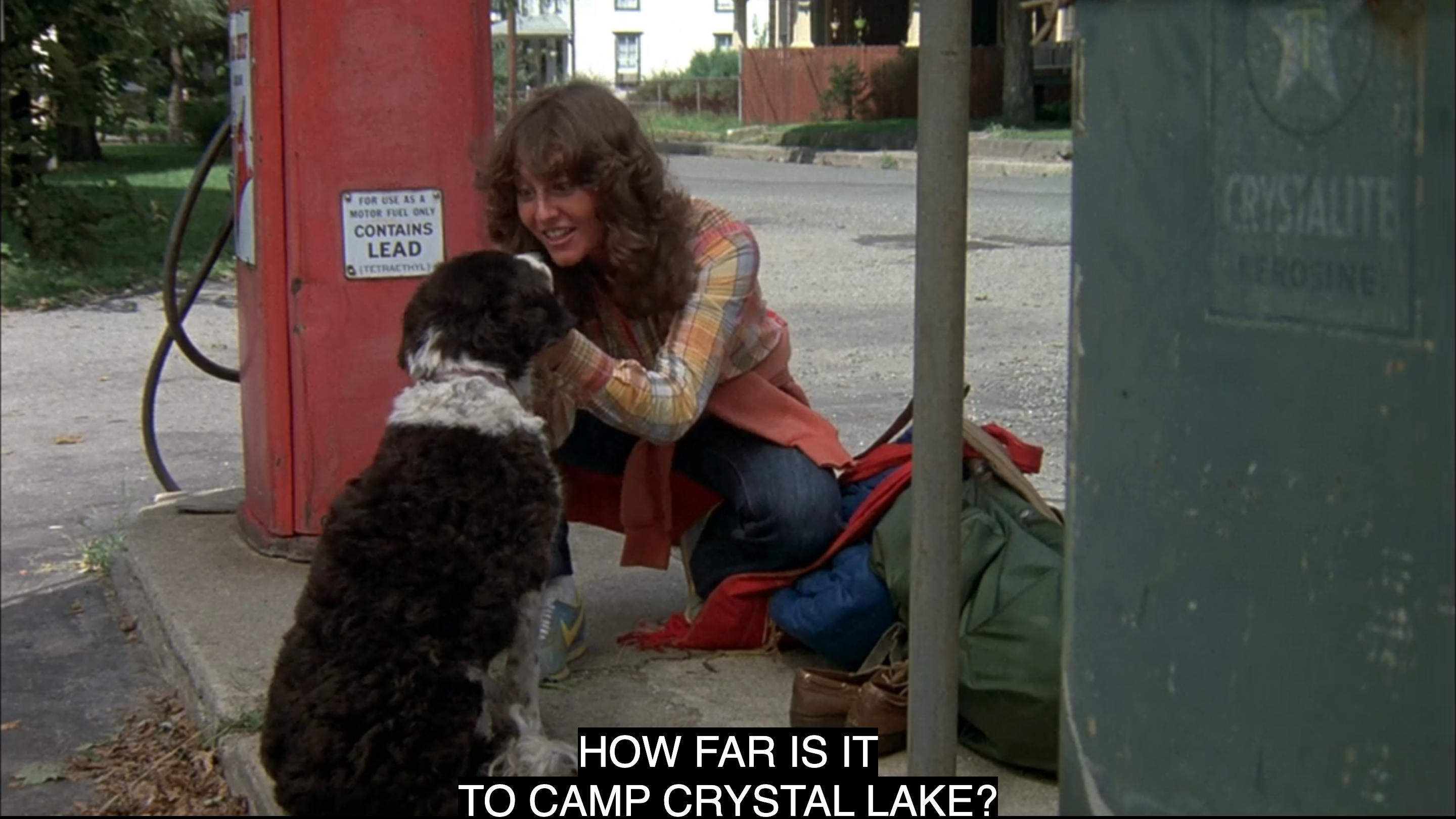 A white teenage girl holds a dog by the ears and says "how far is it to Camp Crystal Lake" in Friday the 13th