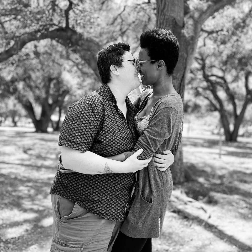 Beth and Sa'iyda embrace in a park in this romantic black and white photo. They're smiling, lips almost touching, like they've just kissed or are about to.