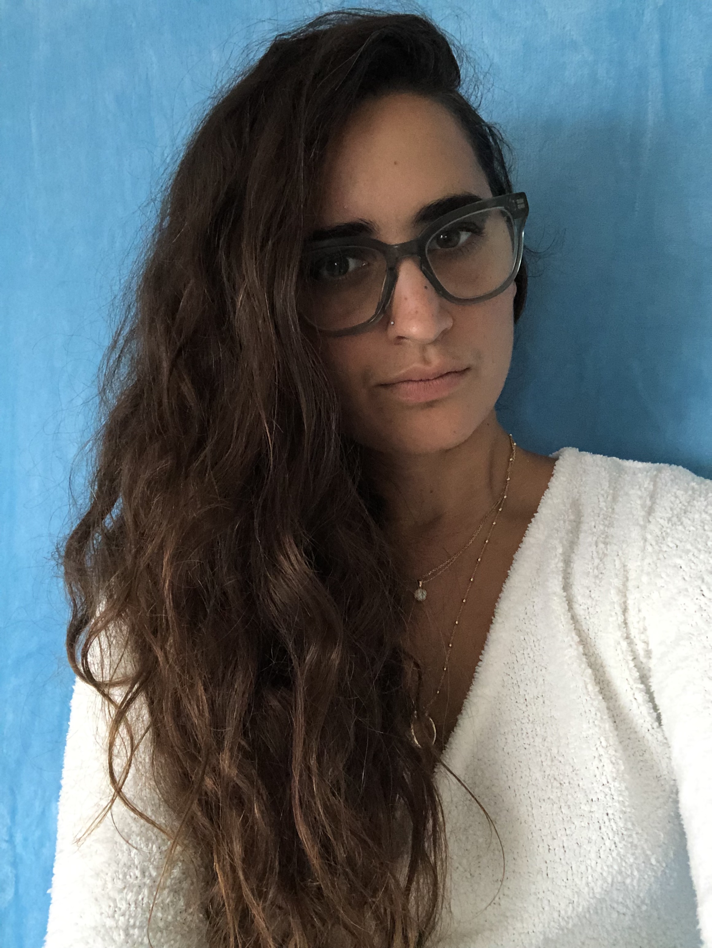 Kayla Kumari Upadhyaya is a brown dyke with long brown curly hair and a white fuzzy shirt on. She wears blue glasses. She probably has "lesbian eyebrows."
