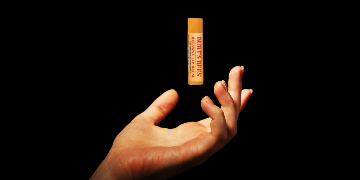 a hand against a black background gently unfolds, palm up. the palm is illuminated. above the palm floats a single tube of Burt's Bees chapstick