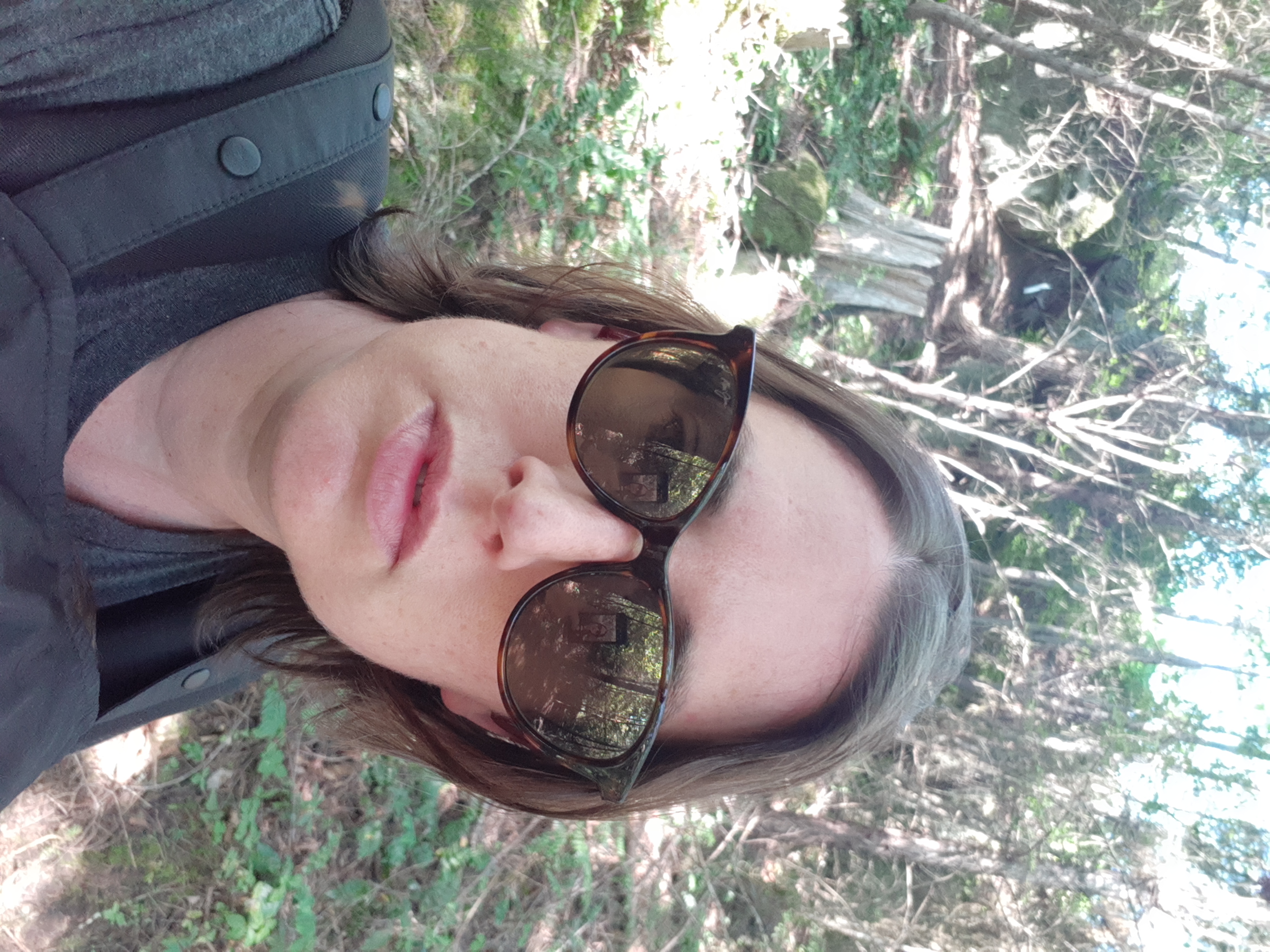 Casey, a white woman, regards the camera with lips parted. She is wearing sunglasses and has short brown hair.