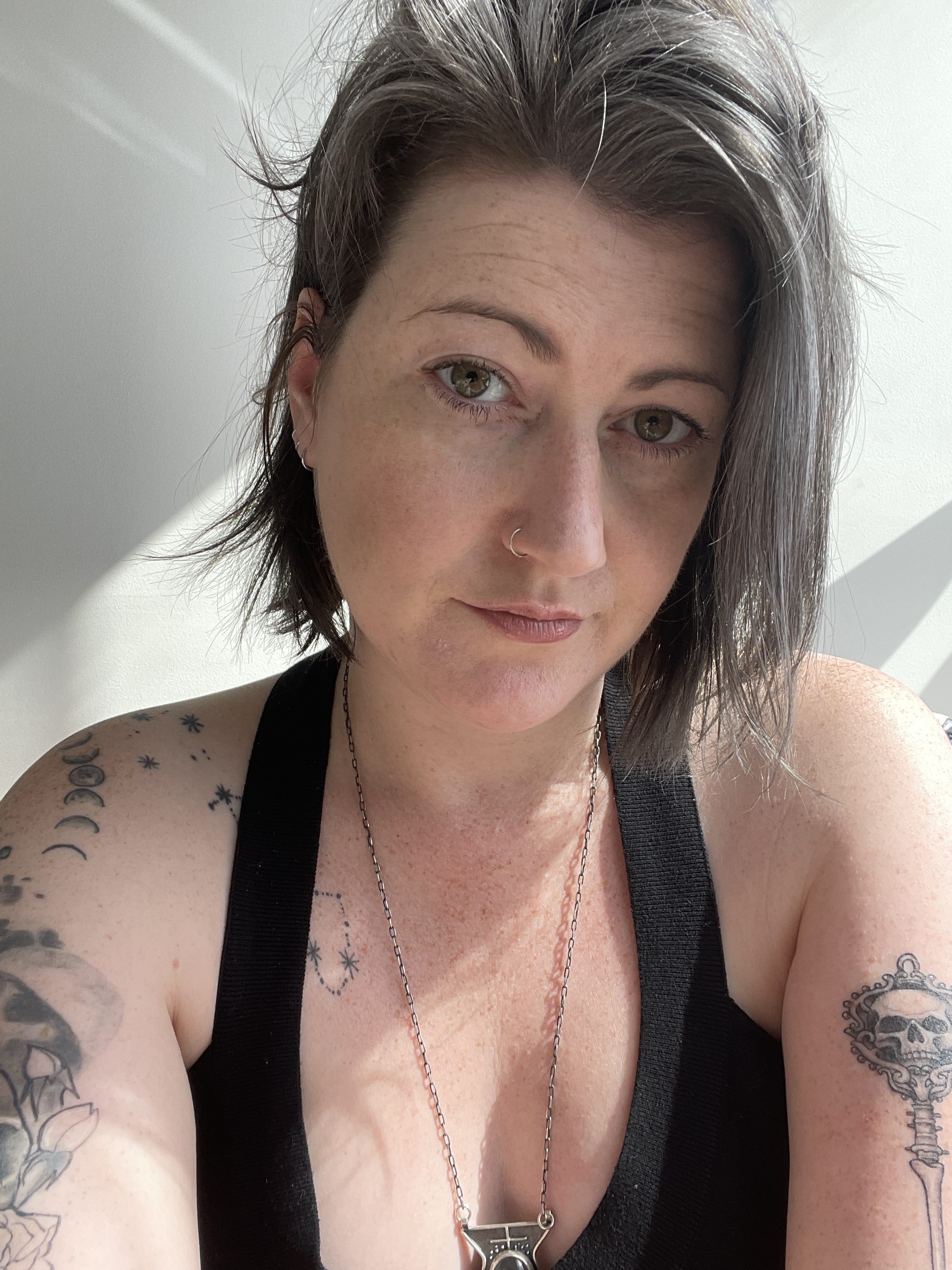 Meg, a white woman, is gazing into the camera, wearing a black tank top. She has a salt and pepper bob.