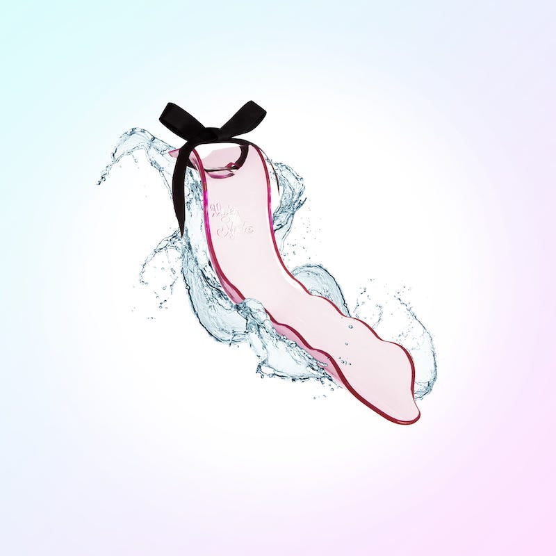 The WaterSlyde, a pink piece of plastic shaped like a slide has a black bow on top, is against a pastel background of pinks, blues, purples and whites. Splashing water is visible around the toy.