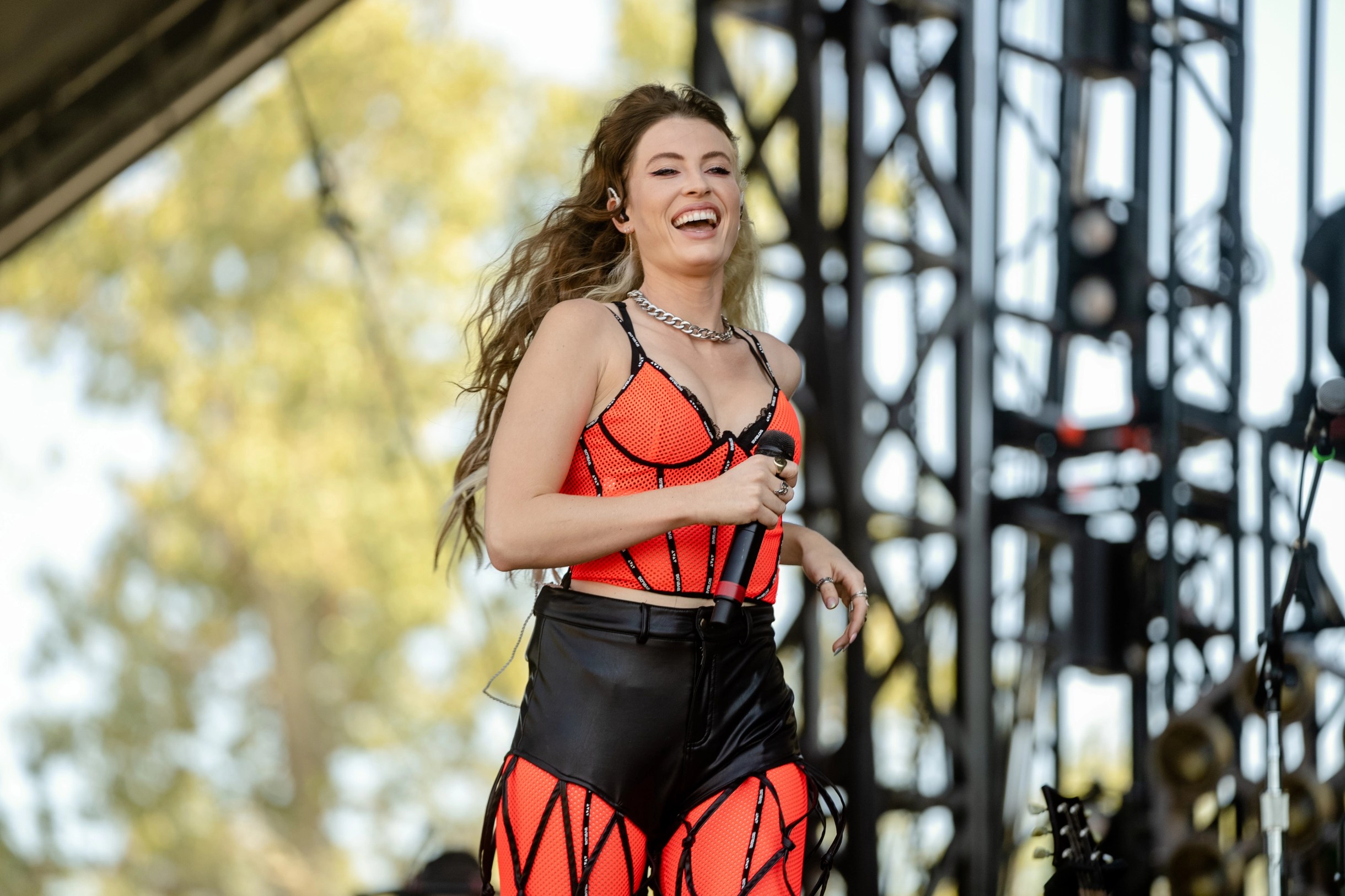 fletcher runs across a stage wearing a show outfit that is like a bright orange red corset with black piping