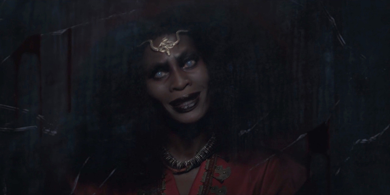 Dominique Jackson as Bloody Mary appears in a dirty mirror. Her pupils are milky and she has a piece of gold jewelry on her forehead.