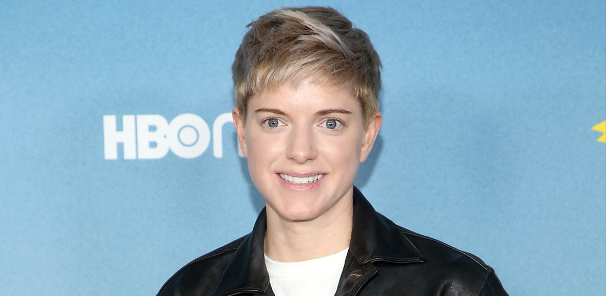 Mae Martin in front of an HBO background on the red carpet of the Hacks premiere