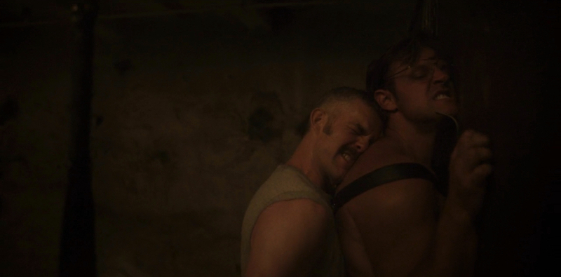 Russell Tovey presses a man against a wall while fucking him in a dark basement.