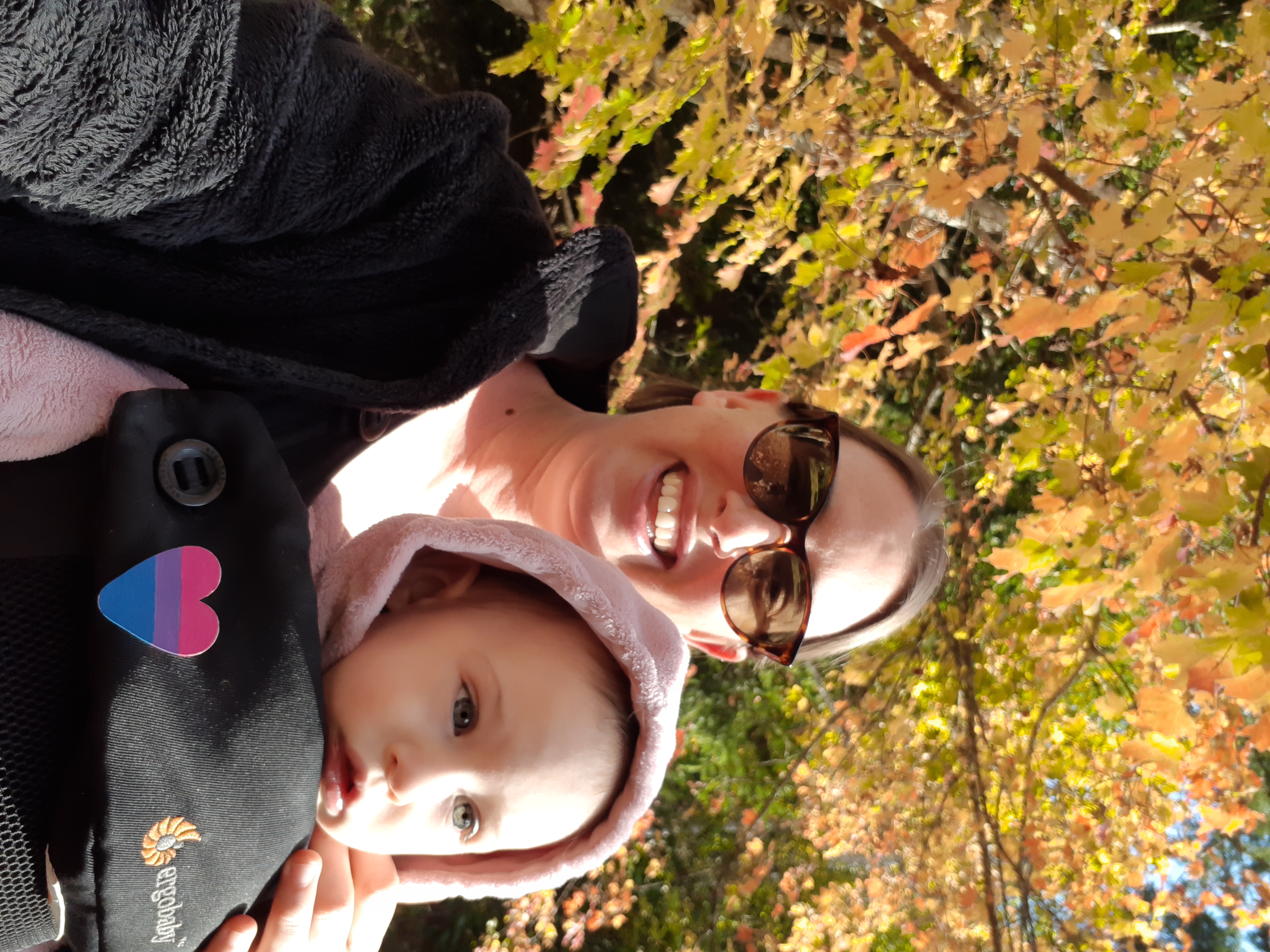 Casey walks outside under fall leaves with her daughter. Case is a white woman with light brown hair who is wearing sunglasses