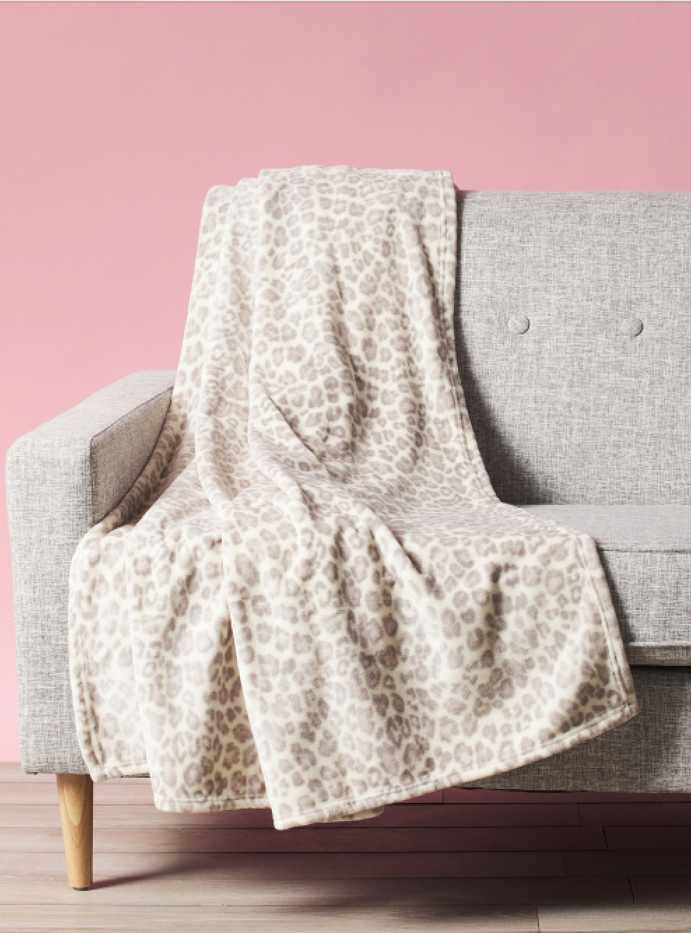 a gray and white leopard print blanket on a gray couch against a pink wall