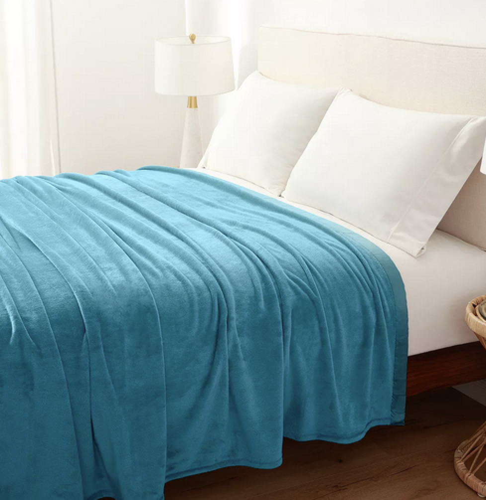 a teal blanket draped over a white bed with big white pillows against a white wall