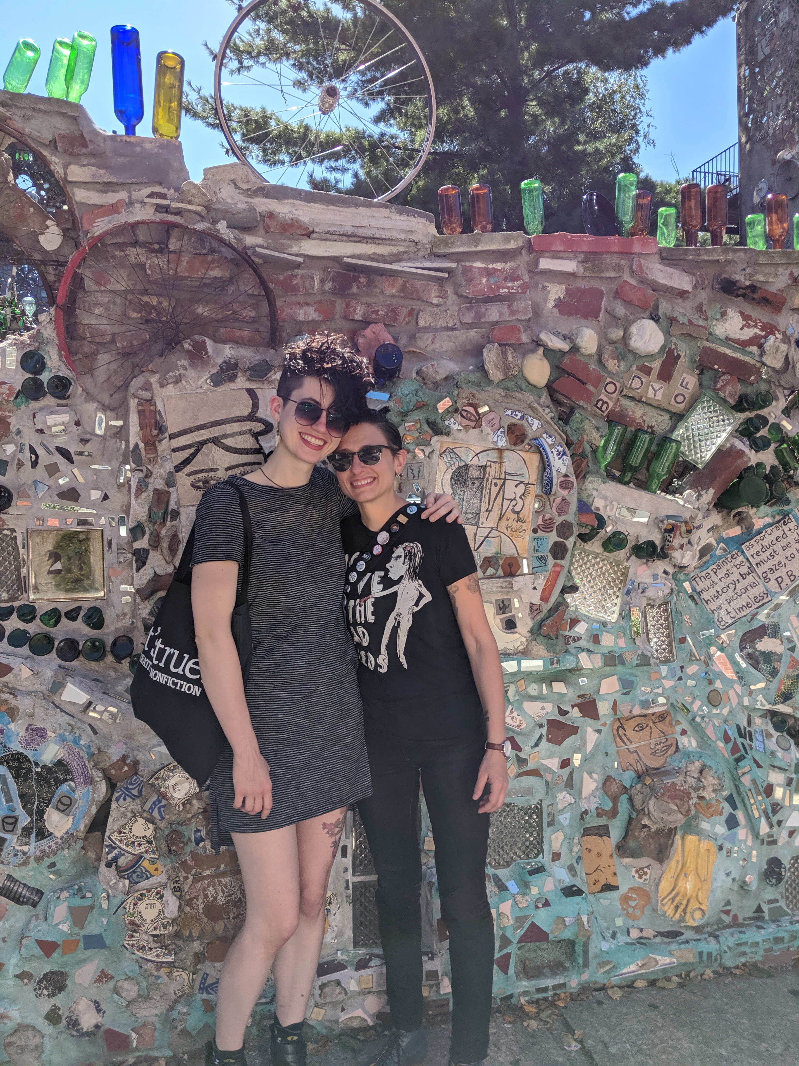 sadie and nico pose on a sunny day in front of the wall to the magic garden in philadelphia
