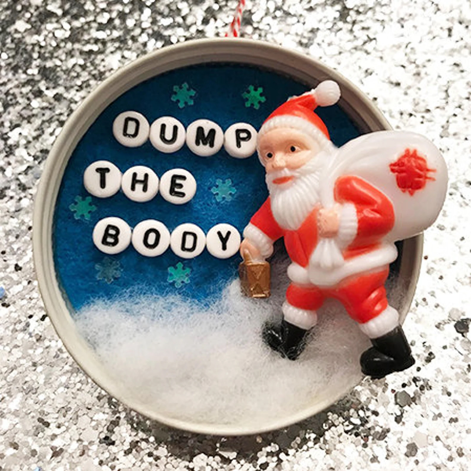a santa ornament where the white toy sack on santa has a red stain on it and lettering on the ornament reads "dump the body"