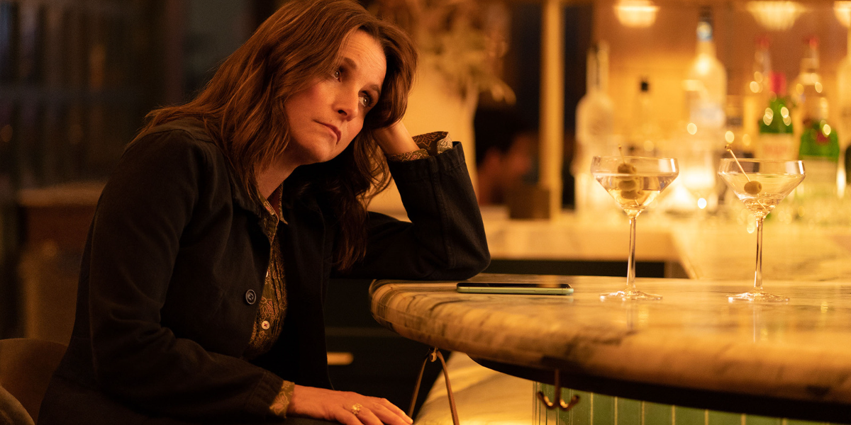 Julia Louis-Dreyfus site at a bar with he head in her hand, looking upset. Her mascara is messy.