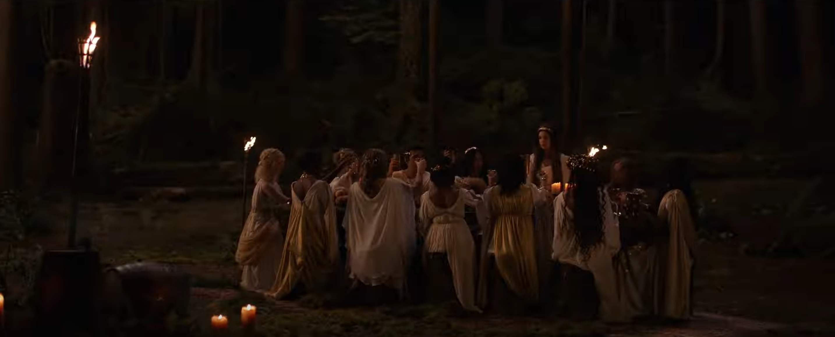 The Yellowjackets characters around a table in the woods wearing white and gold Ancient Greek looking gowns