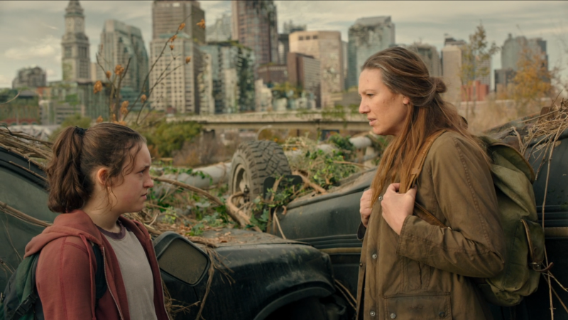 The Last of Us: Tess and Ellie stand and talk with a post-apocalyptic Boston in the background