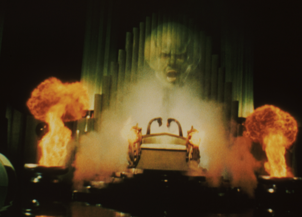 a screen cap of the wizard of oz himself as a giant floating green projected head with lots of smoke