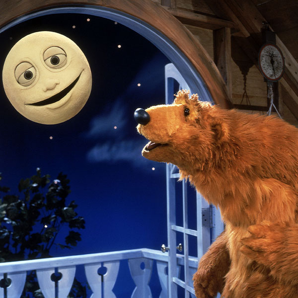 Bear looks out the window and smiles at the moon, who smiles back.