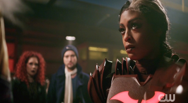 A screenshot of Ryan Wilder as Red Death on the Flash. Ryan is in the foreground and has a gray streak in her hair and is wearing a red batsuit with a broken bat logo. There are two rogues in the background.