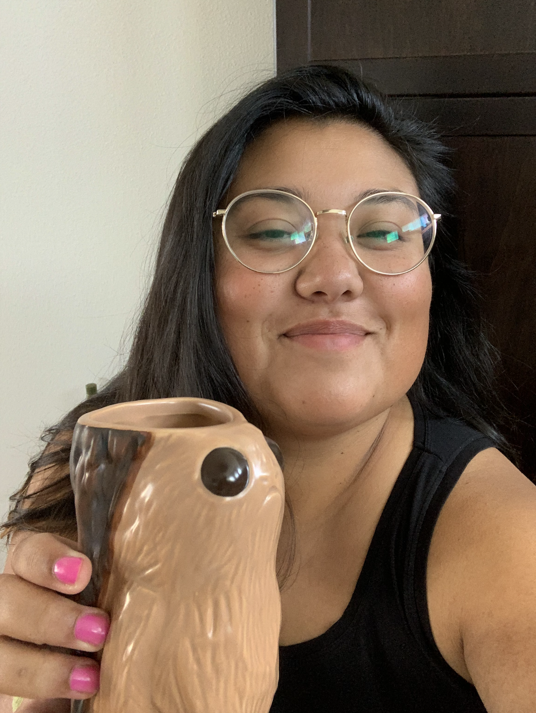 em, a mixed race person with long black hair and glasses holds up what appears to be a cup in the shape of some kind of creature to the camera and smiles
