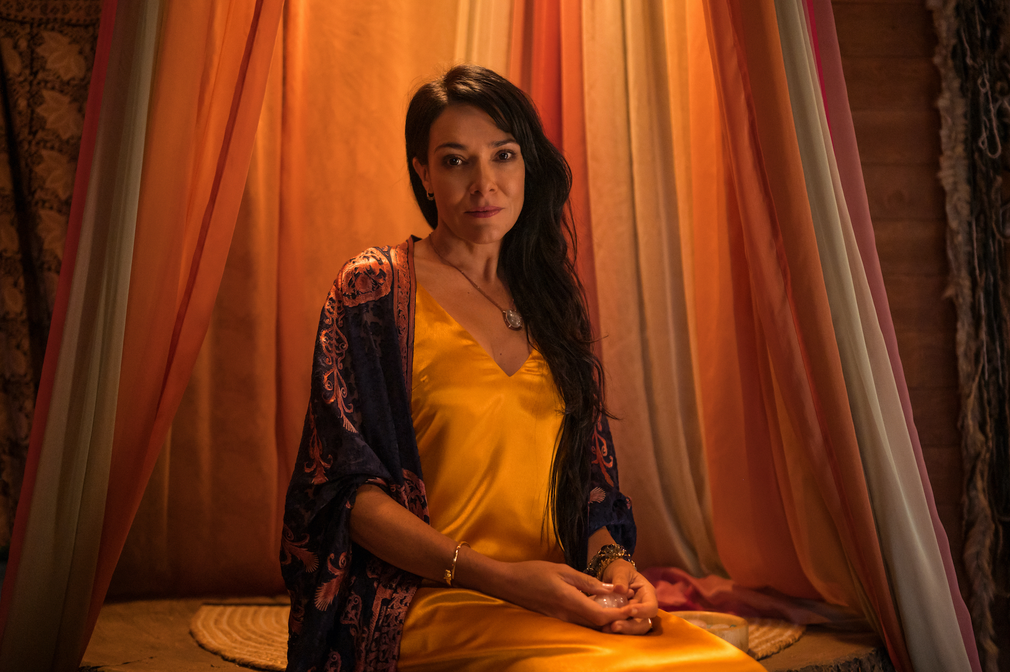 Yellowjackets - Season 2 Simone Kessell as Lottie in YELLOWJACKETS Season 2 sits among colorful drapes. Photo Credit: Kailey Schwerman/SHOWTIME.