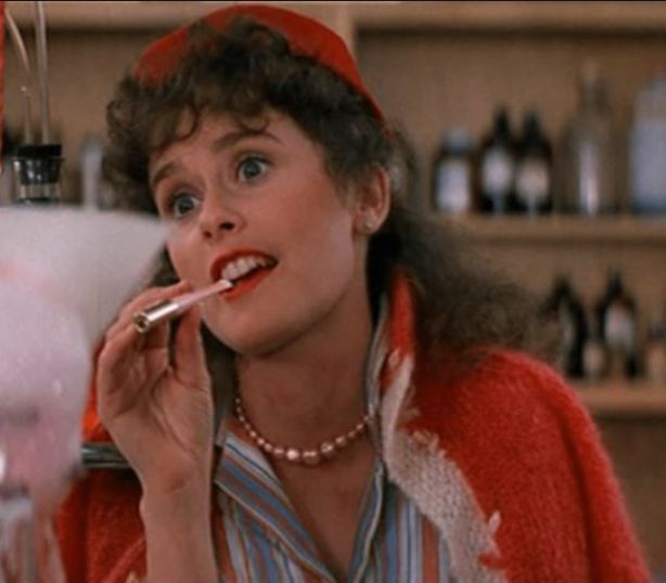 Sharon in Grease 2, wearing red jacket and pillbox hat with a long cigarette in her mouth