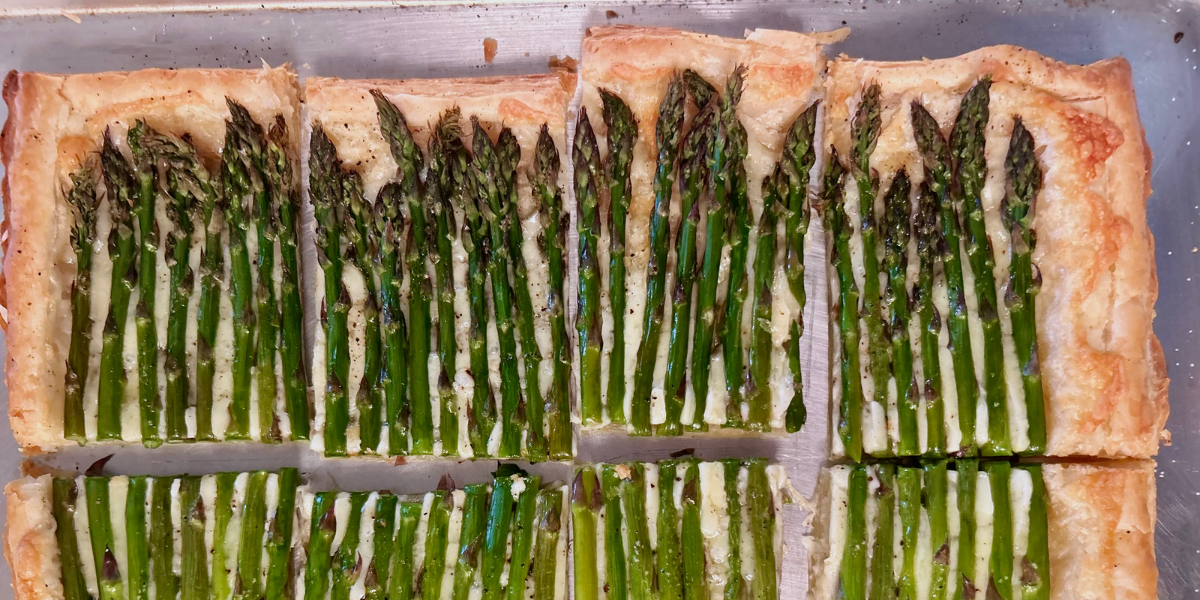 A four-ingredient asparagus tart, in a close up photo. Asparagus spears are sitting in a cheese and puff pastry shell.