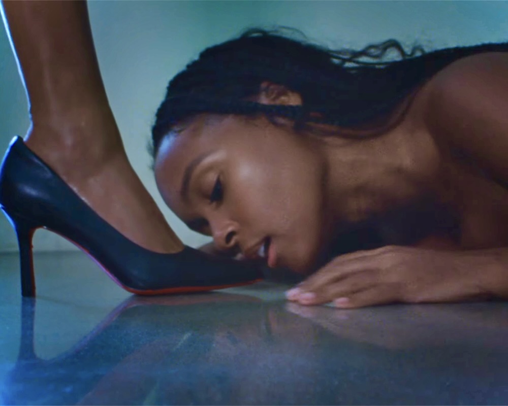 Janelle Monáe sings to a high heel, about to lick it.