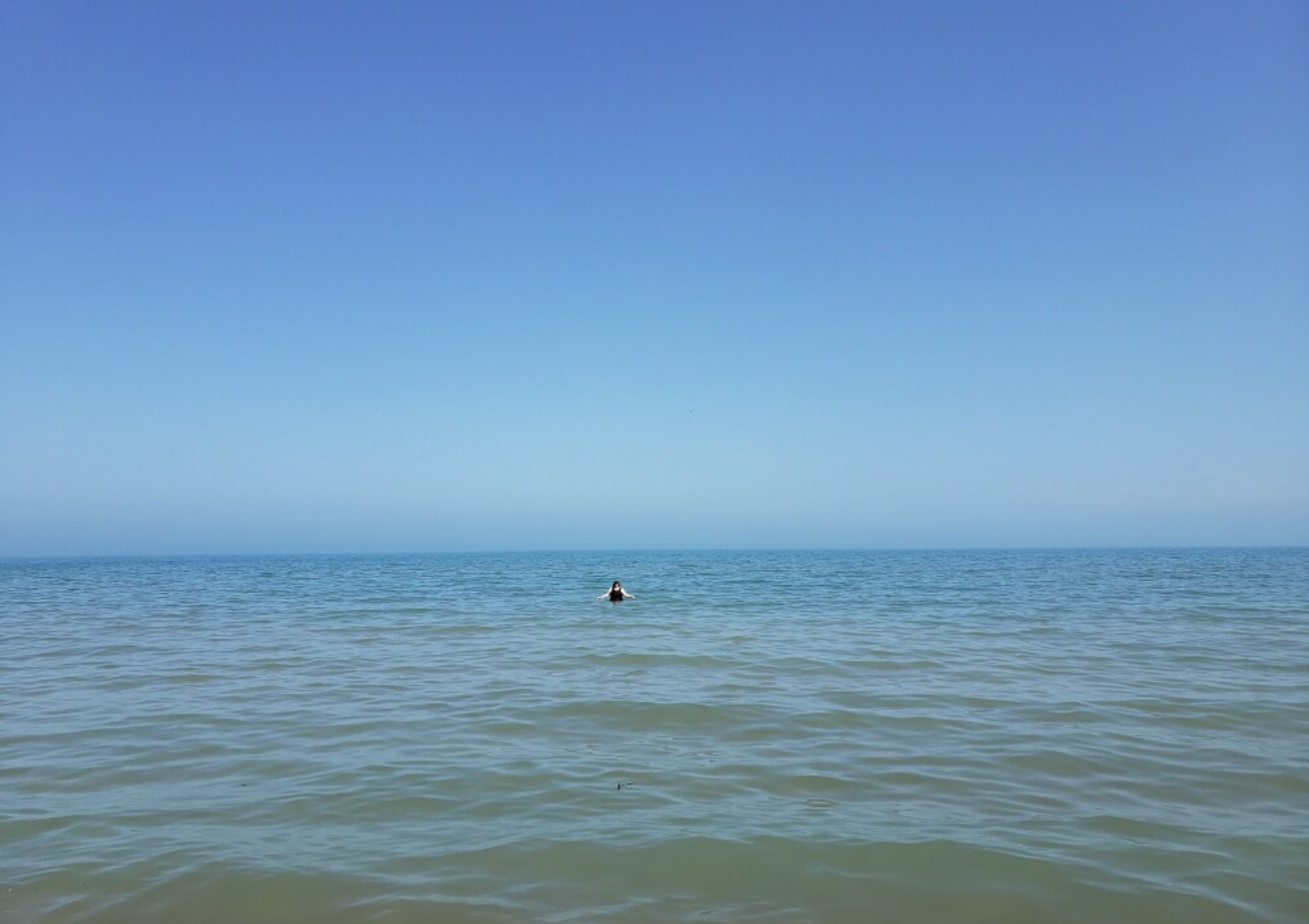A tiny speck of a person in a huge blue lake, with blue water above them