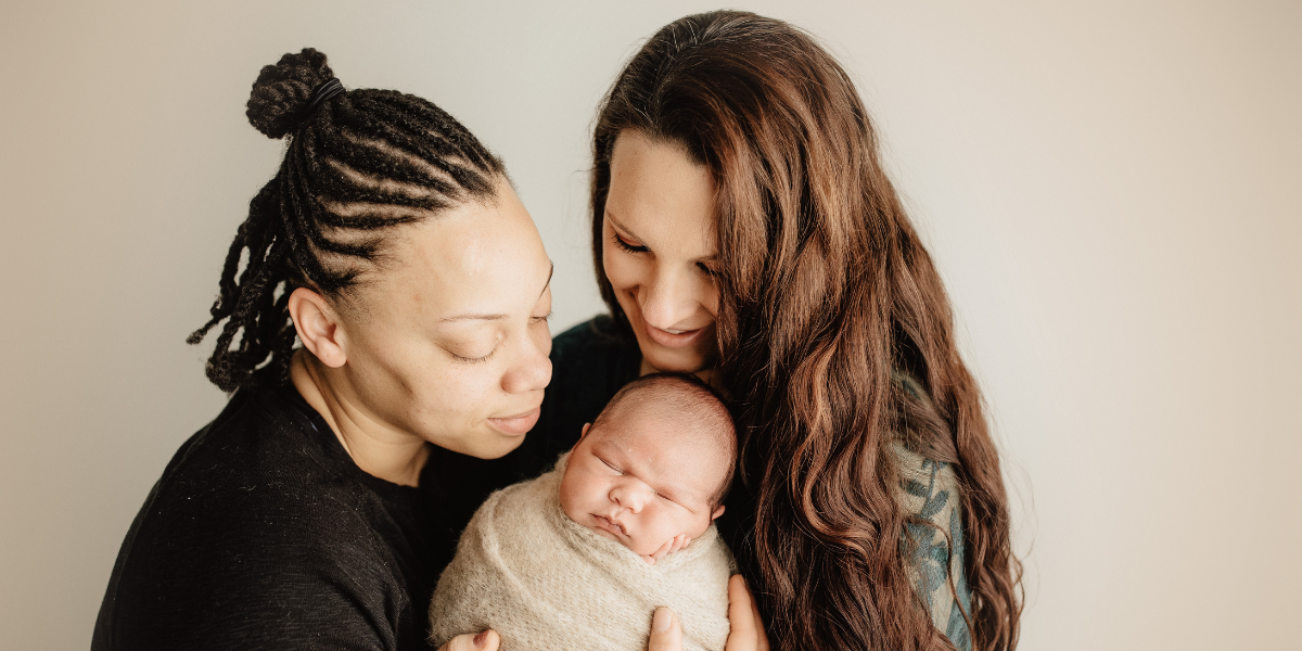 two women hold a swaddled baby