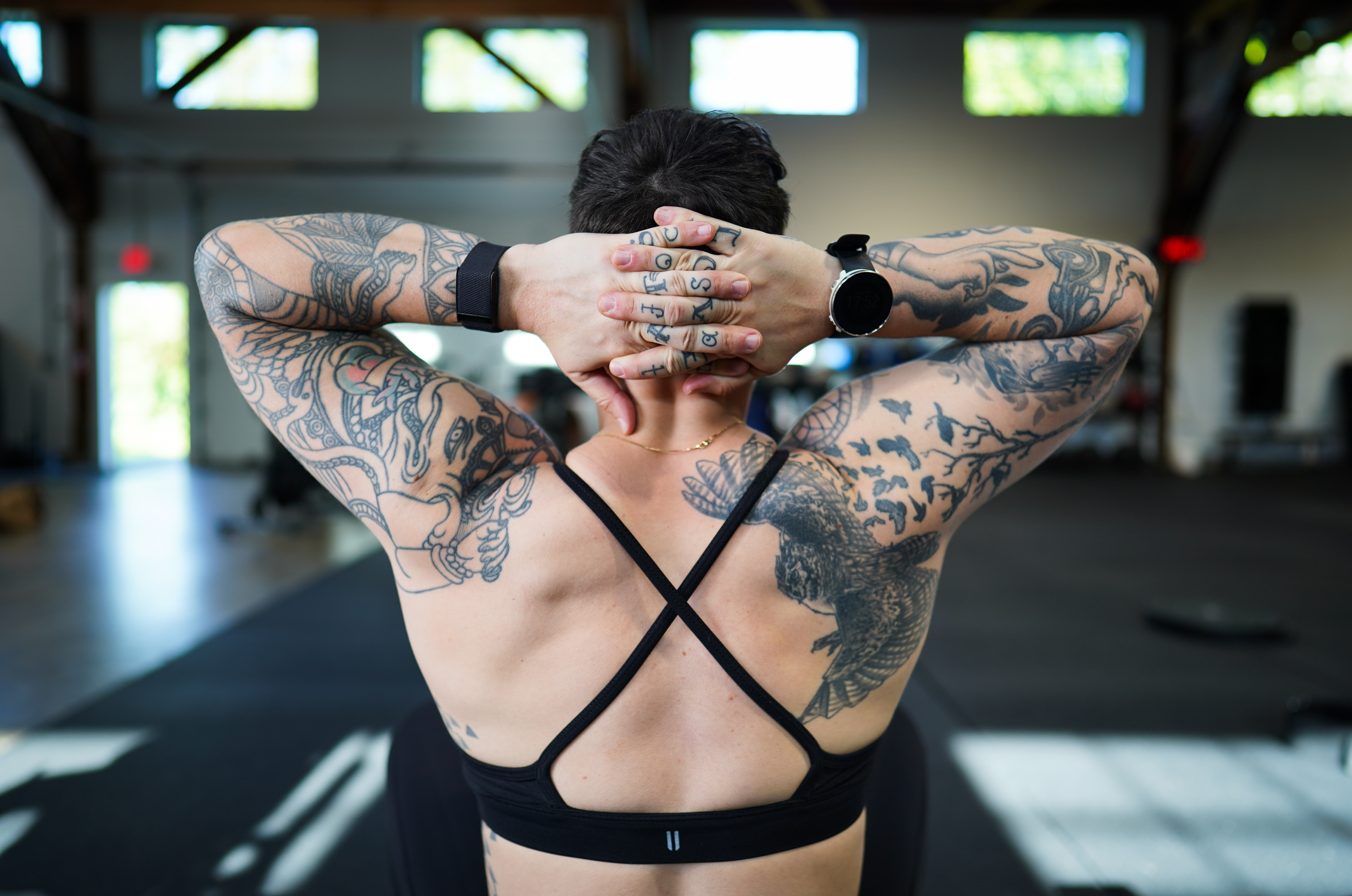 from behind, a shot of a white butch with a lot of tattoos wearing a black sports bra
