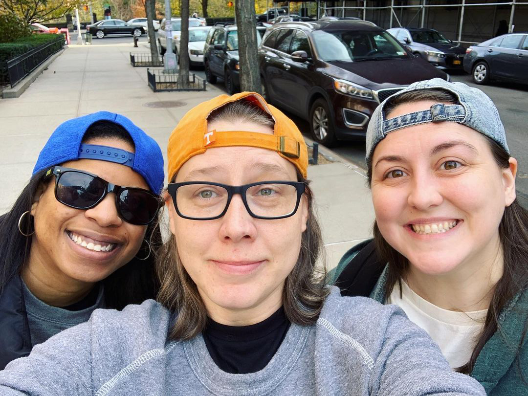 Nic, Heather, and Valerie in backwards hats hanging out on the street.