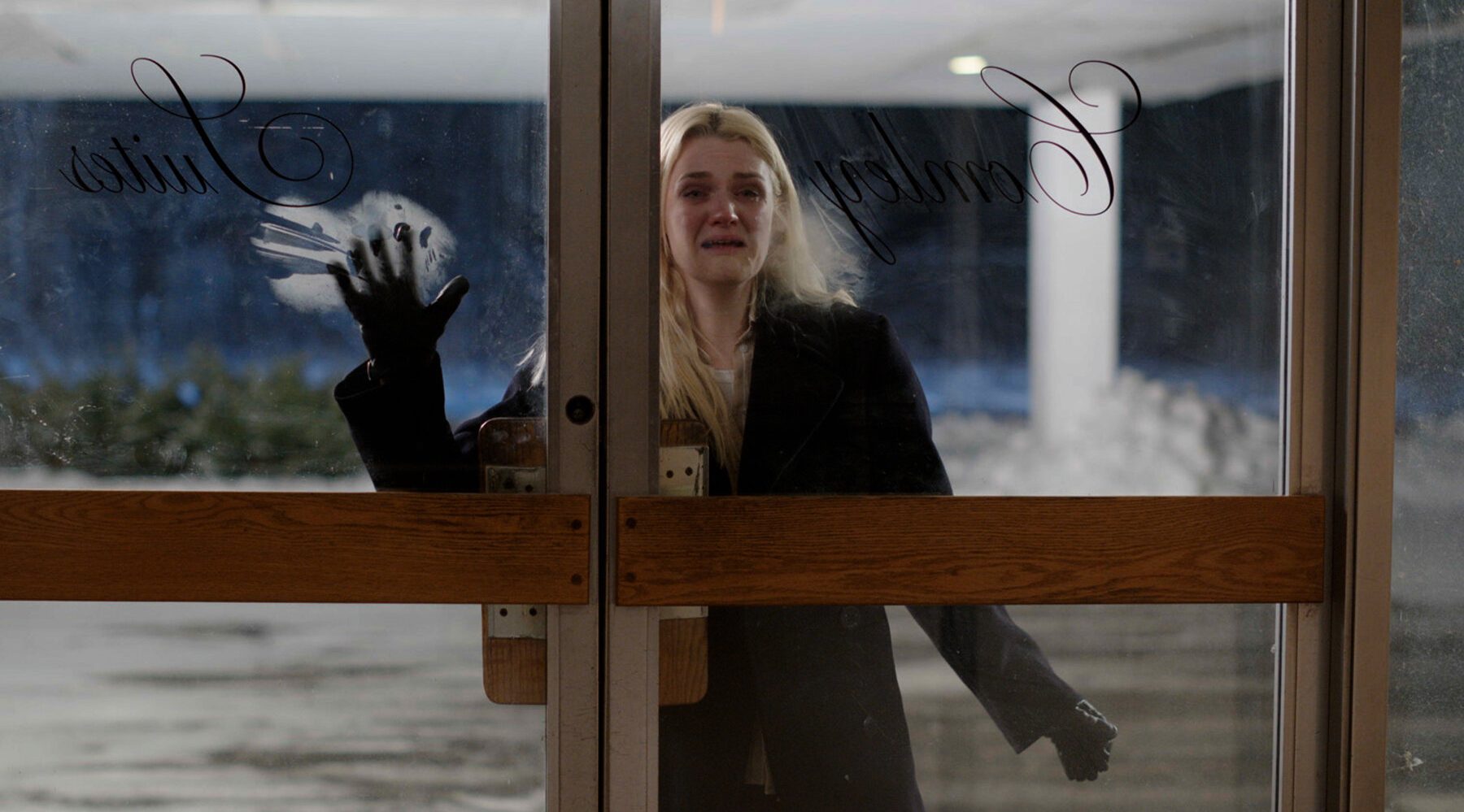 Queer horror to stream: Bad Things. Gayle Rankin covered in blood stands at the automatic front doors of a small hotel.
