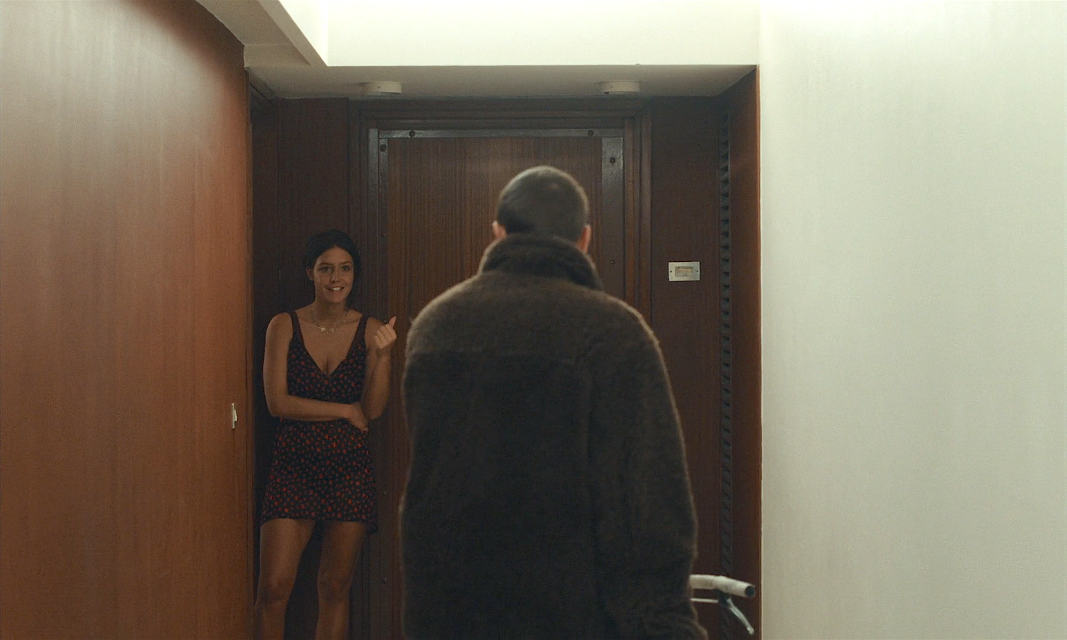 Adèle Exarchopolous wearing a black mini dress with a rose pattern stands in a hallway greeting a man.