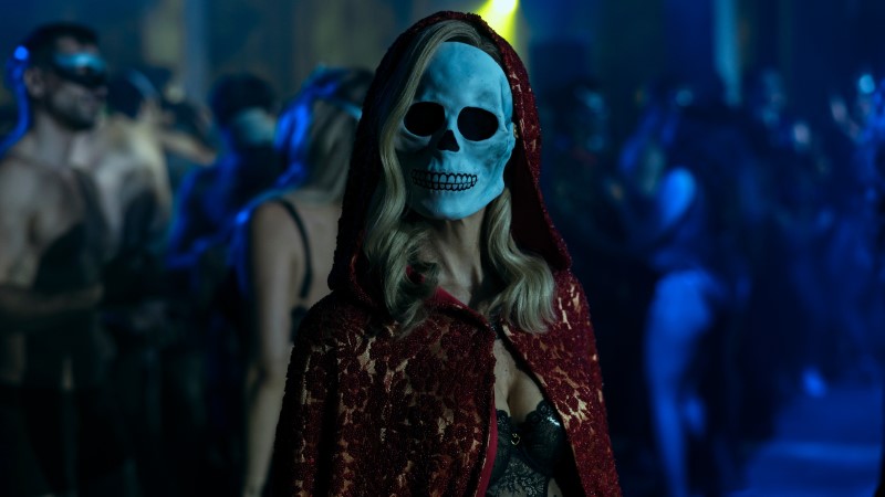 A woman dressed in lingerie, a red sparkly cloak, and The Masque of the Red Death
