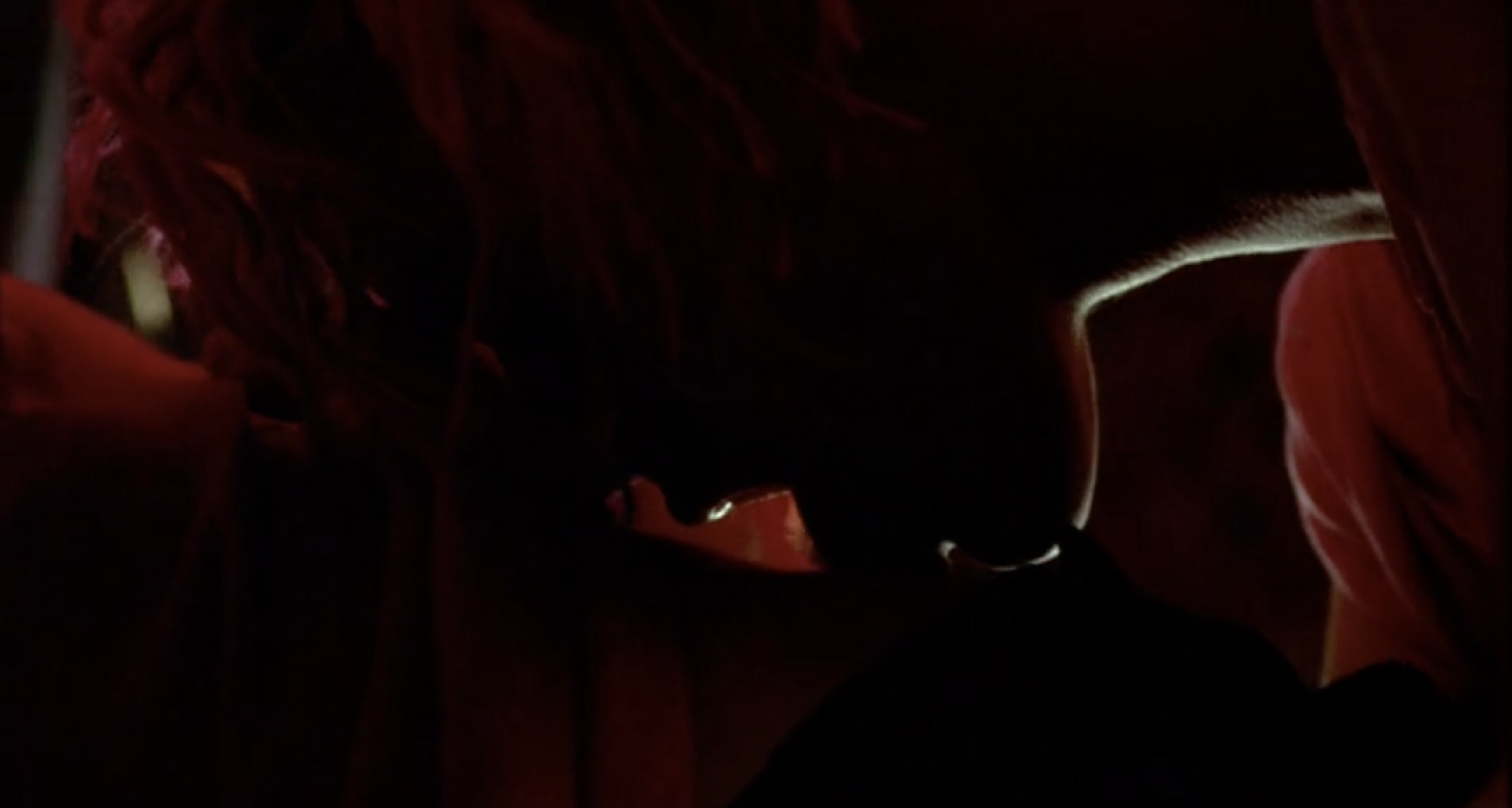 Sexy lesbian screenshot: Leisha Hailey with pink hair in very low lighting licks another woman's back.