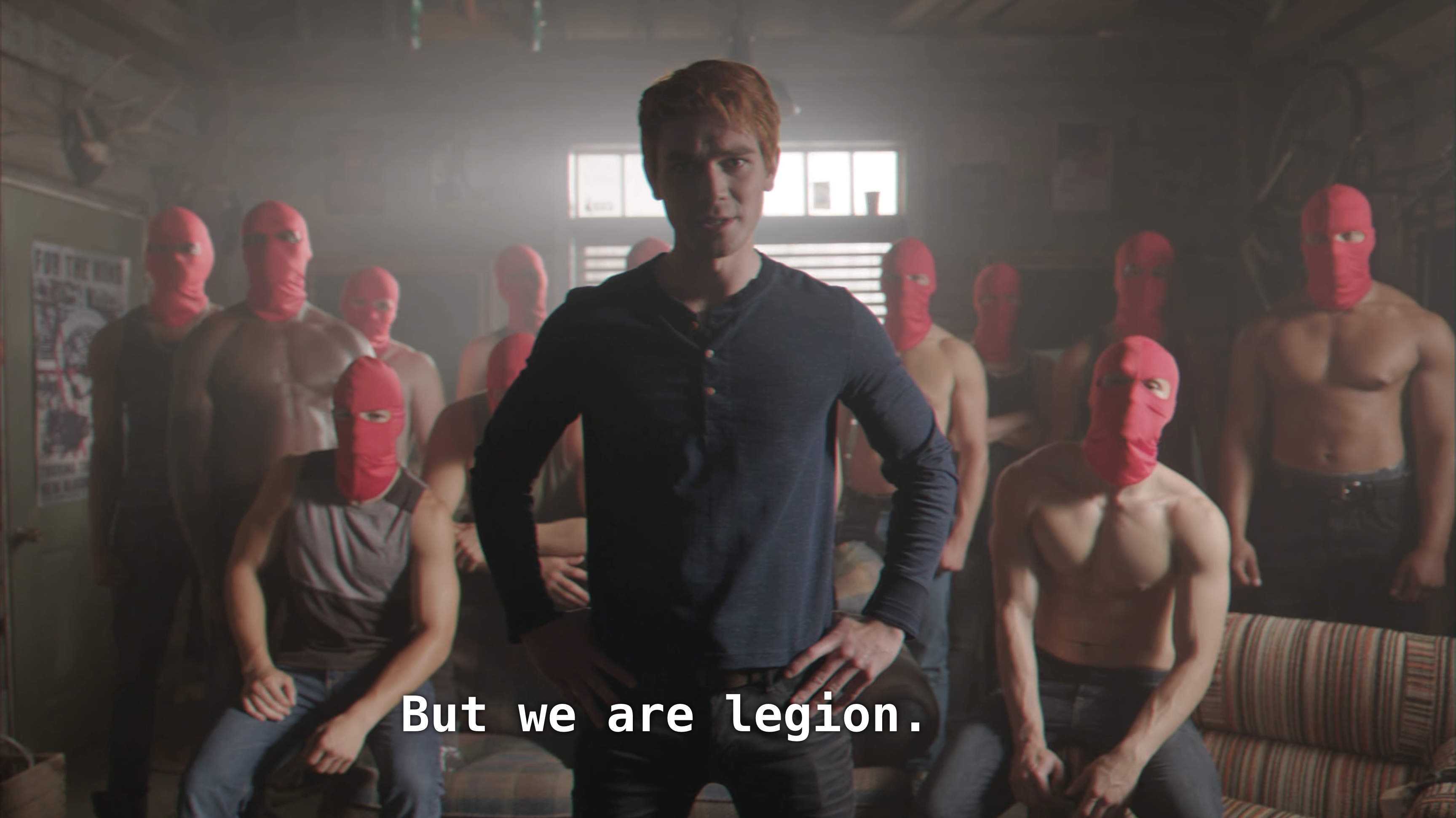 Archie stands with his hands on his hips, shirtless boys behind him in pink balaclavas
