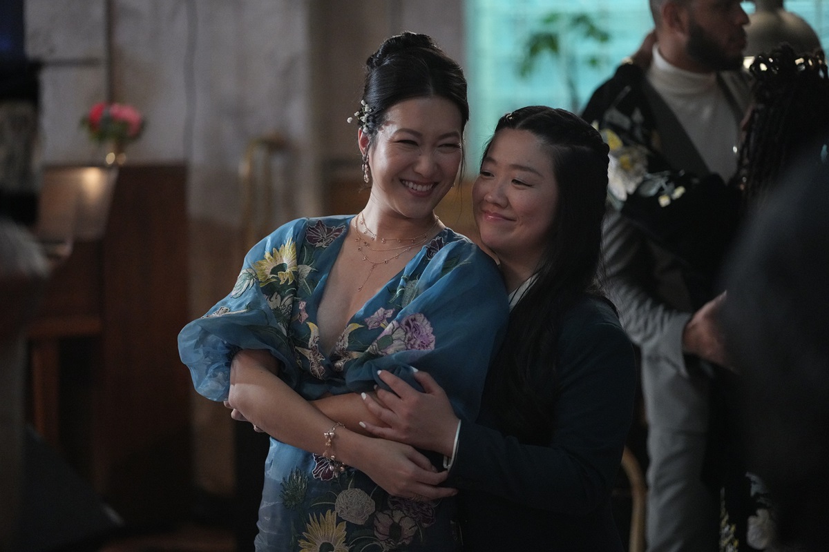 Alice and Sumi dance together at Callie's engagement party after acknowledging that one day marriage will be in their future. Sumi is wearing a blue floral print midi dress and she's pressed up against Alice who's in a suit.