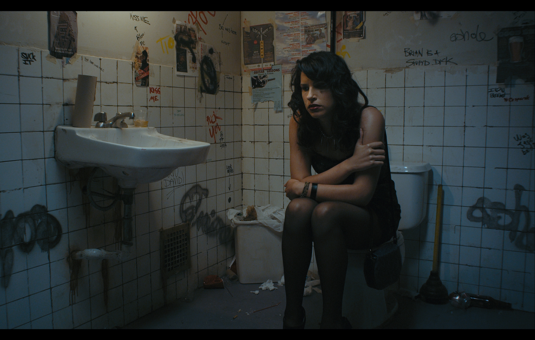 A Persian woman in her 20s is sitting on a toilet and she is very sad