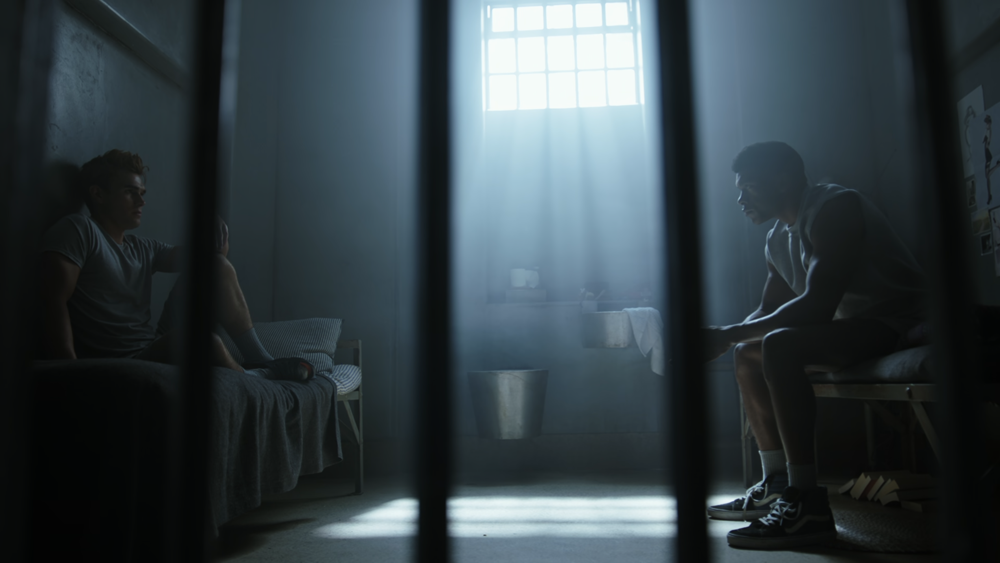 Archie and Mad Dog sit on opposite sides of a prison cell.