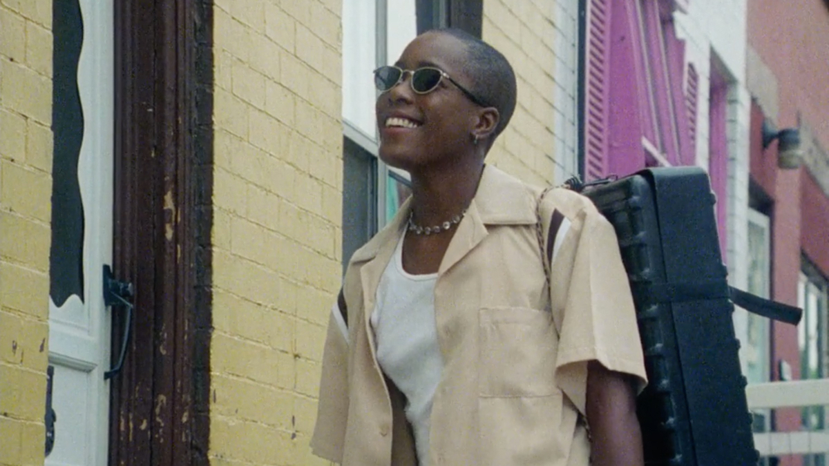 Best lesbian movies #2: Cheryl Dunye in sunglasses and tan shirt over a white tank looks up smiling.