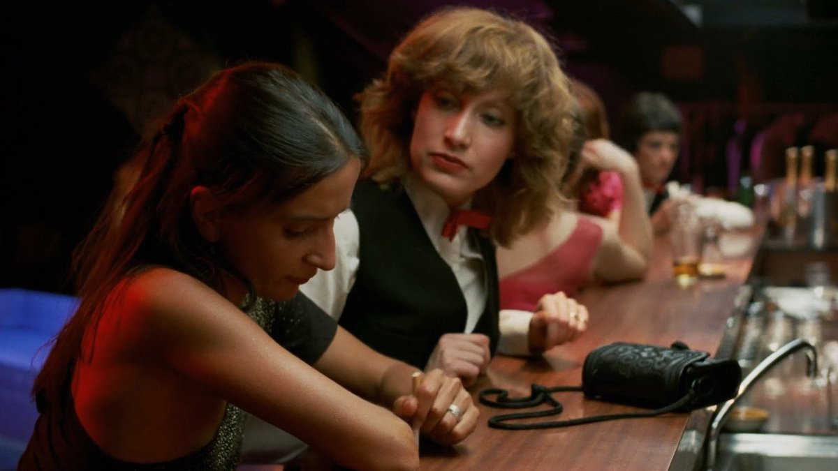 A female bartender looks at another woman sitting at the bar with her head down.