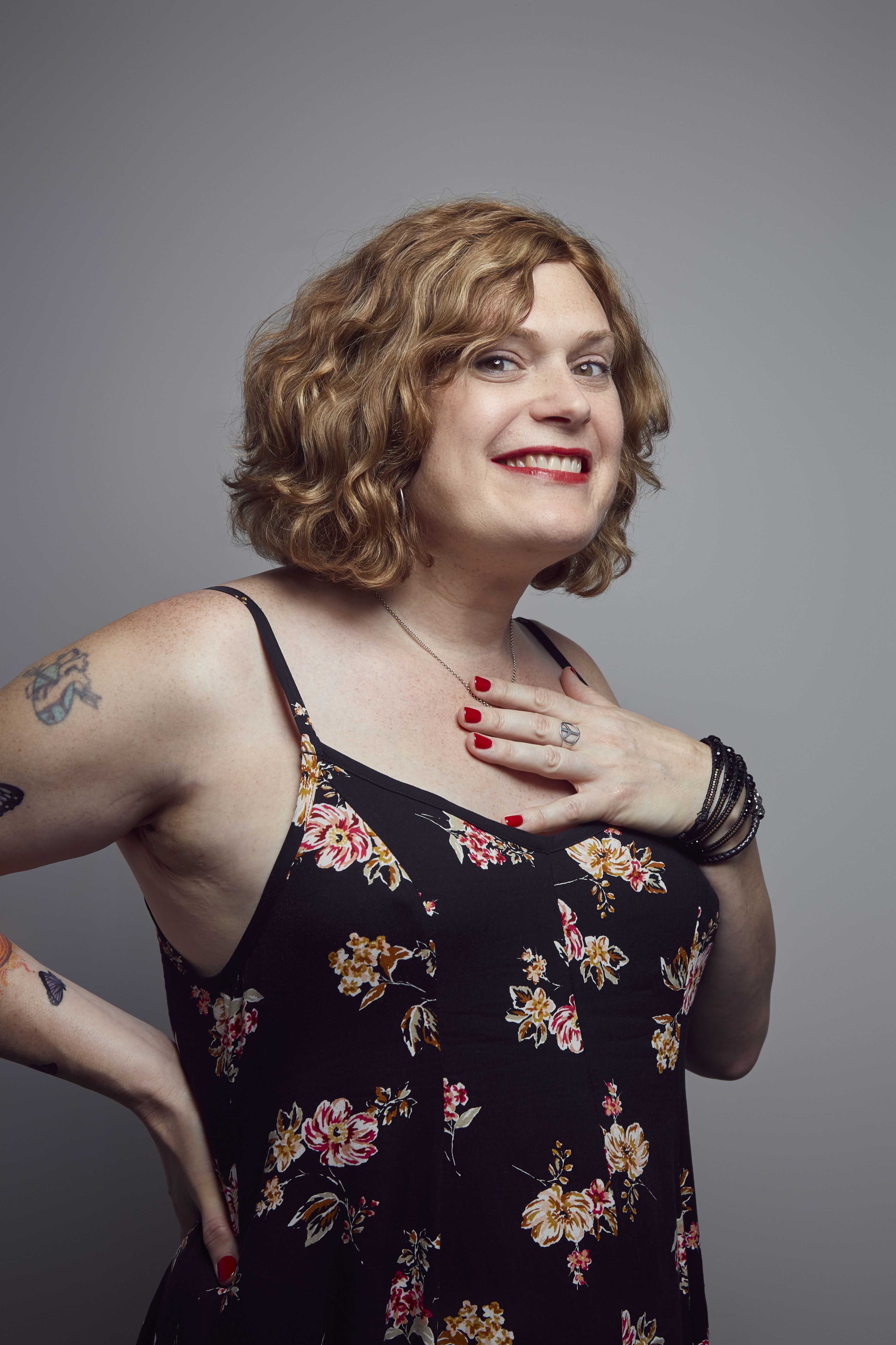 Lilly Wachowski interview: Lilly poses with one arm on her back and another on her chest smiling at the camera in a black dress with a flower print.