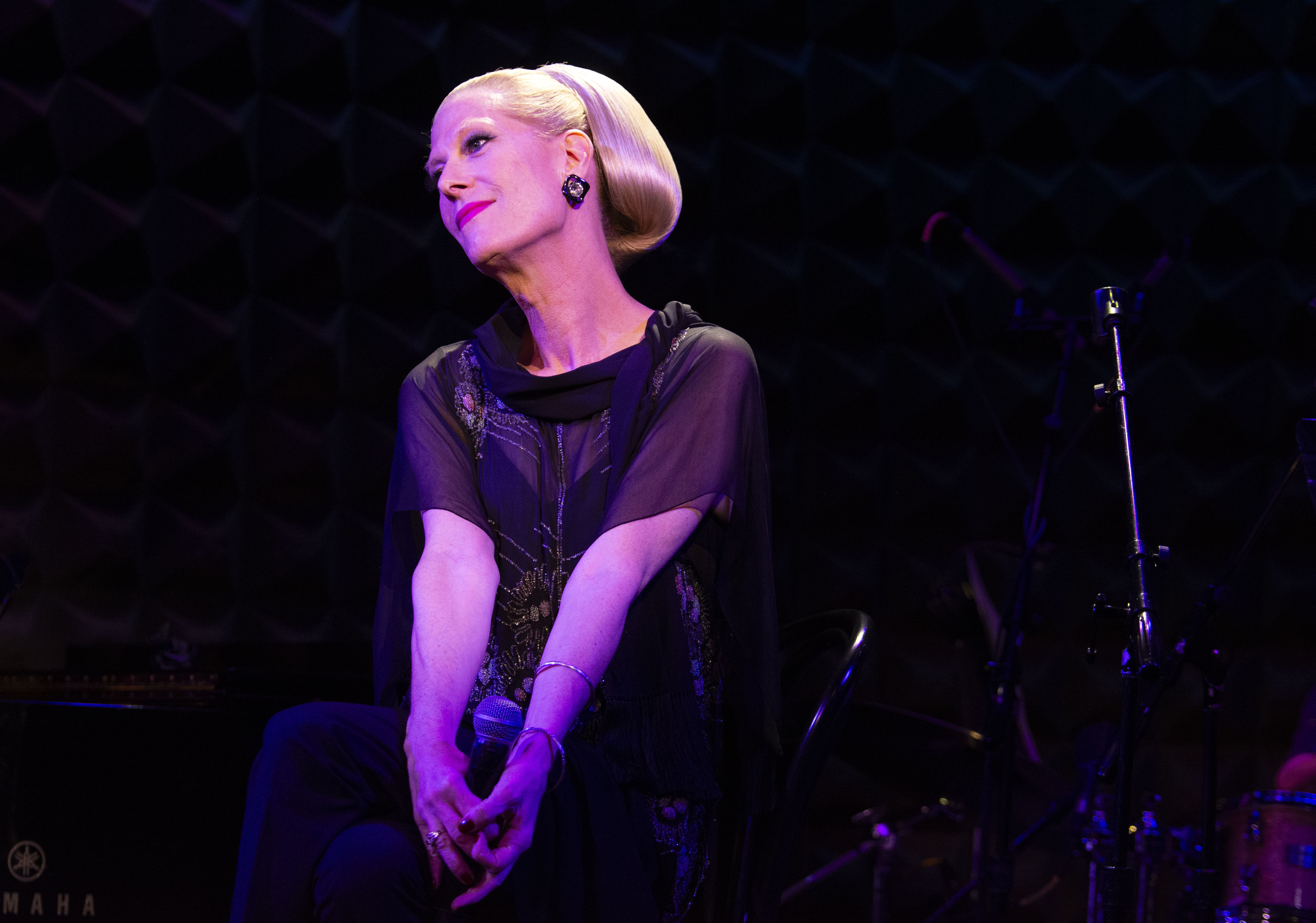 Justin Vivian Bond sits demurely holding a microphone on stage