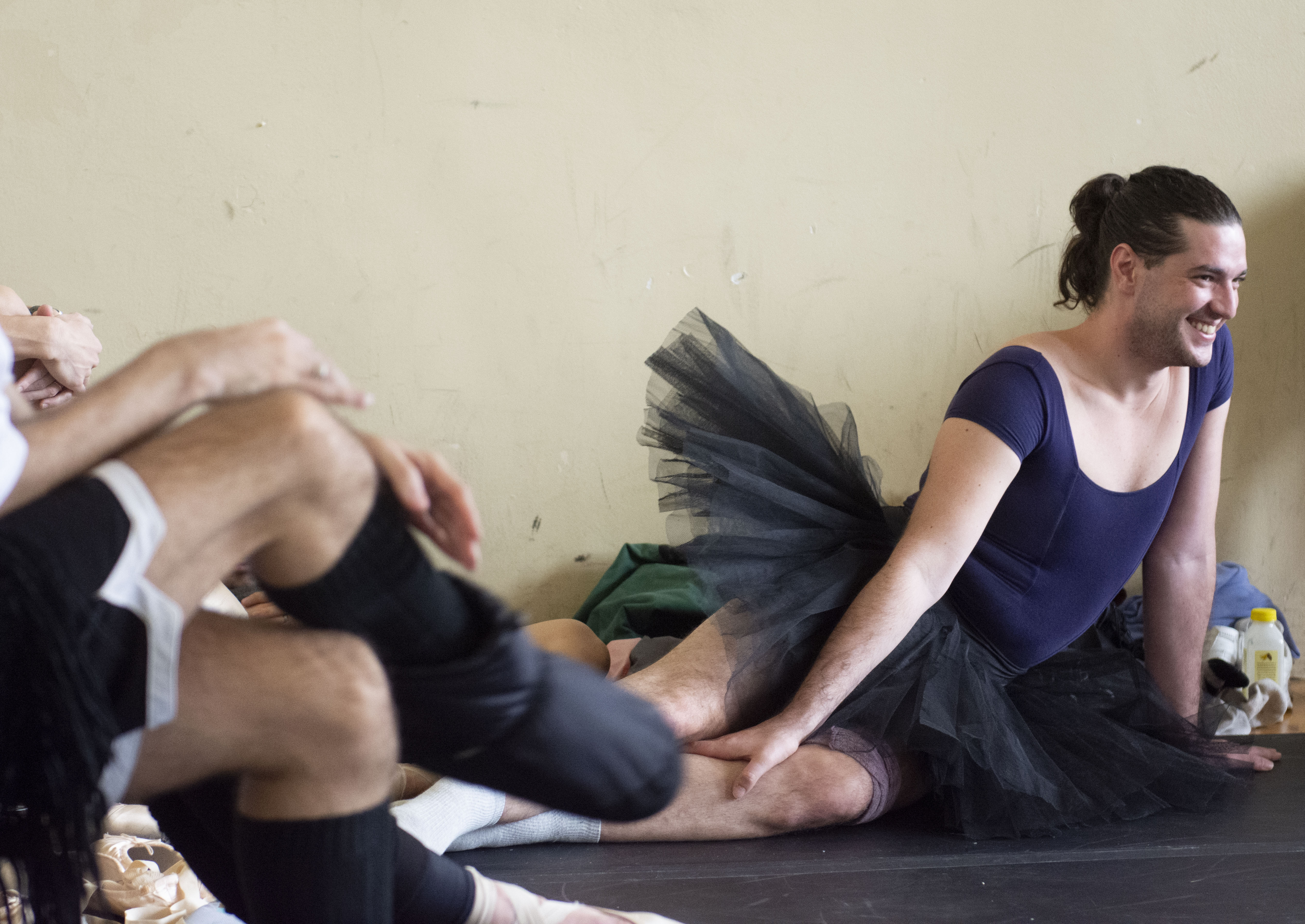 Andrea Fabbri smiles and stretches in a black tutu on the floor.