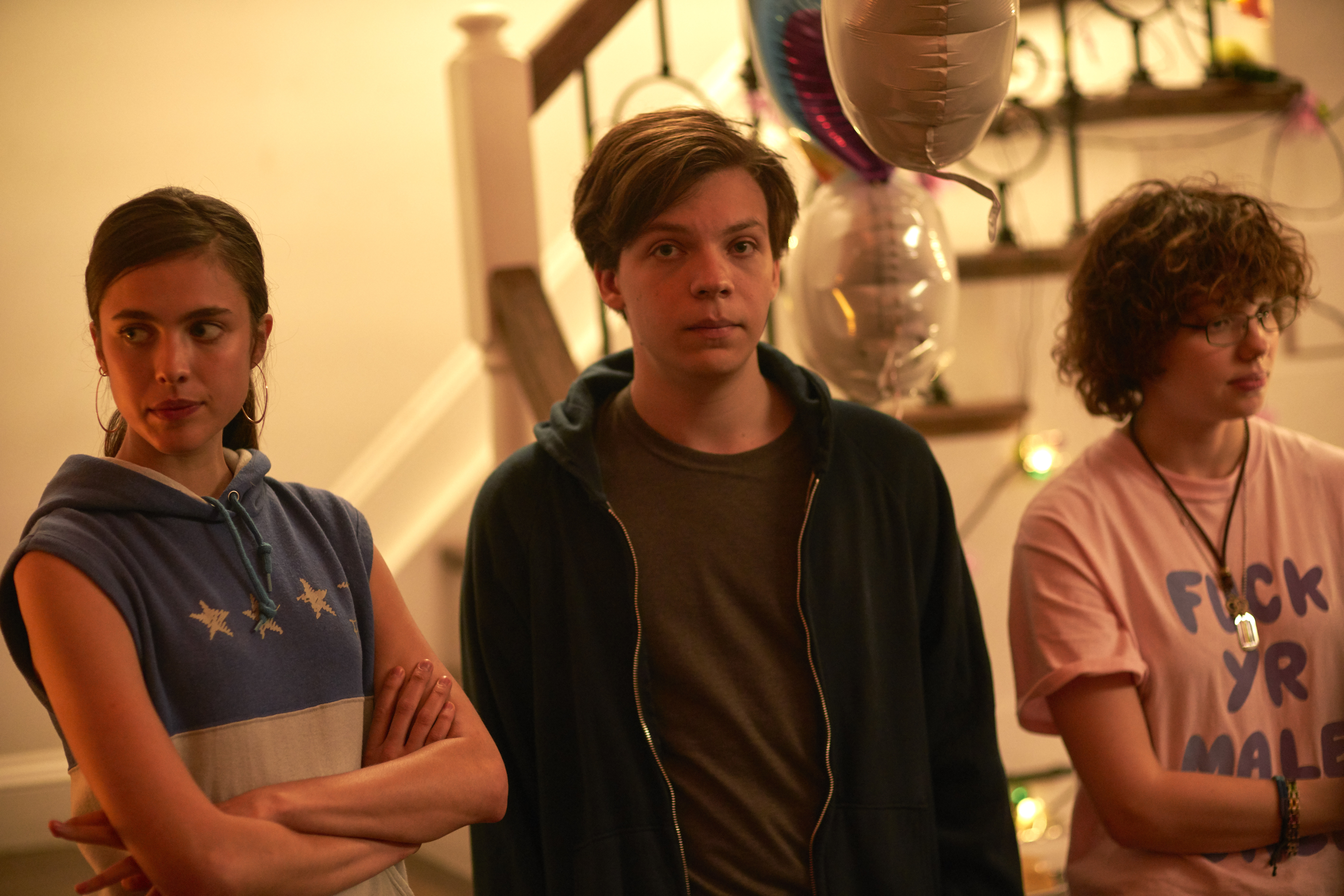 Margaret Qualley, Nicholas Braun, and Chloë Levine stand awkwardly next to each other during a party scene